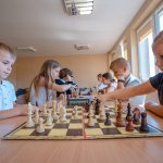 Młodzi szachiści - chłopiec w szarej bluzce polo i dziewczynka w granatowej bluzeczce grają w szachy